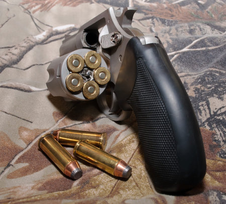 A loaded, stainless steel 44spl revolver on a camouflage background with it's cylinder opened and...