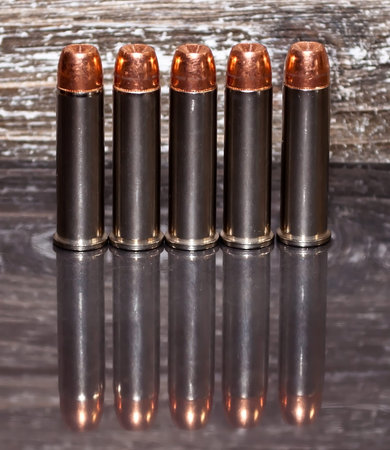 Five .357 magnum bullets lined up with a wooden background and on a reflective surface showing the...