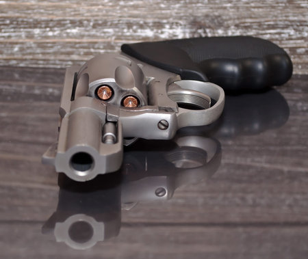 A loaded, stainless steel .357 magnum revolver on a reflective surface with a wooden background