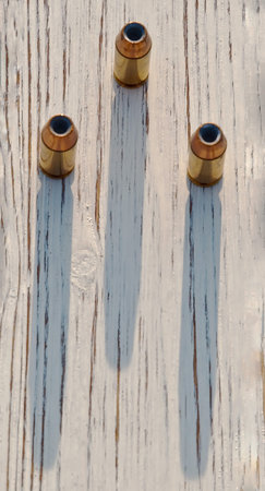 Three hollow point 40 caliber bullets on a wooden table casting their shadow upon the table