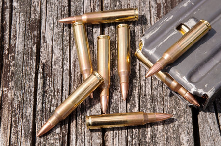 A loaded metal rifle magazine with seven .223 bullets next to and on top of it on a wooden...