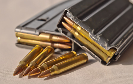 Two metal rifle magazines, one stacked upon the other, loaded with .223 caliber bullets with four additional bullets of the same caliber in front of themの写真素材
