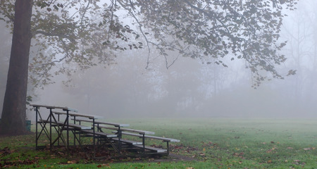 A foggy, fall morning at a soccer field with bleachers under a tree in Frick Park, Pittsburgh, PA, USAの写真素材