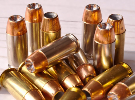 Fourteen different 40 caliber hollow point bullets together on a white wooden background. The...