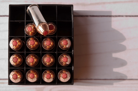 Fifteen 44 special bullets with red tips in a case with one of the bullets on top and several open spots in the case on a wooden background shot from above.の写真素材