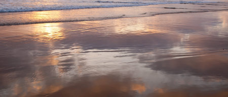 The shallow surf of the Pacific ocean in southern California, USA with the clouds reflecting off the...
