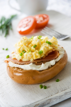 Toasted bagel with ham, cream cheese, chives and scrambled egg topping の写真素材
