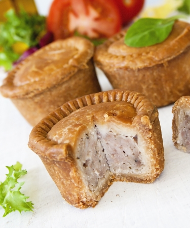 Crusty English pork pie sliced against a background of pies green leaf salad and tomatoesの写真素材