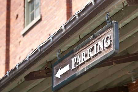 A closeup of a custom parking sign with a directional arrow, hanging from the roof of a building.の写真素材