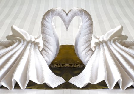 design of double white swans towels on yellow cloth in hotel roomの写真素材