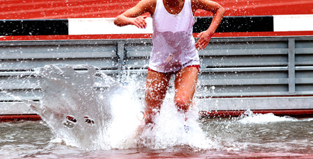 A high school girl running in the steeplechase race landing in the waterの写真素材