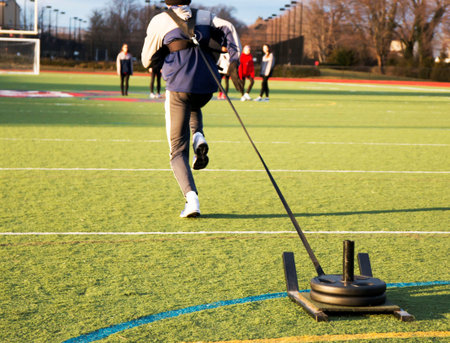 Track and field sprinter pulling a weighted sled on a green turf field during sprinting practiceの写真素材