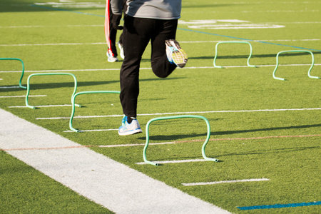 A runner sprints over small green hurdles on a green turf field in the winterの写真素材