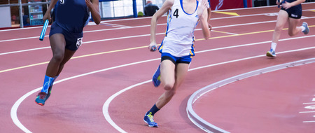 High school girls running in a relay race on a banked track, indoors.の写真素材