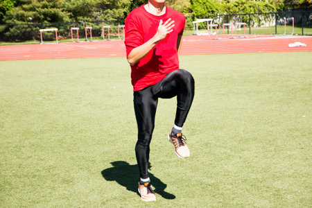 A sprinter perfoming A-Skips on a green turf field warming up for track and field practice