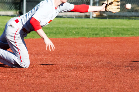 A shortstop dives fot the ball during a baseball game on a red turf infieldの写真素材