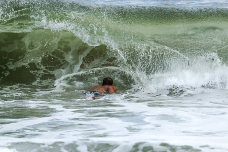 A surfer has to go under a wave, as it curls over him, to be able to get out further into the atlantic ocean off of Fire Island New York.の写真素材