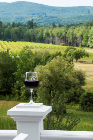 Lincolnville, Maine, USA â 4 August 2017: A wine glass with red wine and the Cellardoor Winery's logo in the foreground and the actual vineyard in the background.のeditorial素材