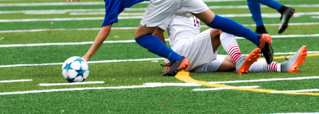 A high school soccer player using a slide tackle on his opponent during a game on a green rutf field.の写真素材