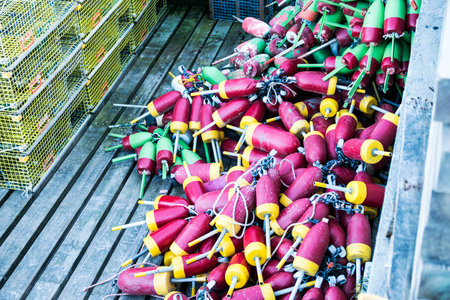 Yellow lobster traps and many different colored buoys are stored on a dock ready to be placed in the...