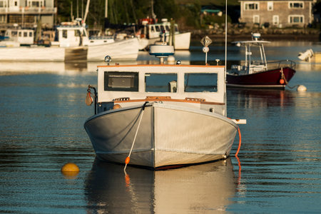 The front view of a white wooden boat with brown trim, moored in Bass Harbor Maine at dusk.