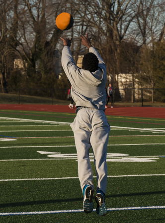 An african american male track and field athlete is tossing a medicine ball foward as he jumps foward as part of strength and speed training in the winter on a green turf field.の写真素材