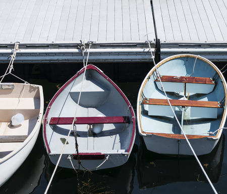 Three colorful row boats are in a perfectly straight line tied up to a dock in New England, Maine.の写真素材