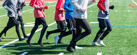 High school boys take their shoes off and jog on the turf in their socks on a sunny, but cold winter...