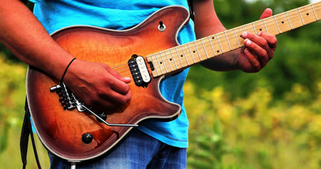 Close up of hands playing an electric guitar while outside.