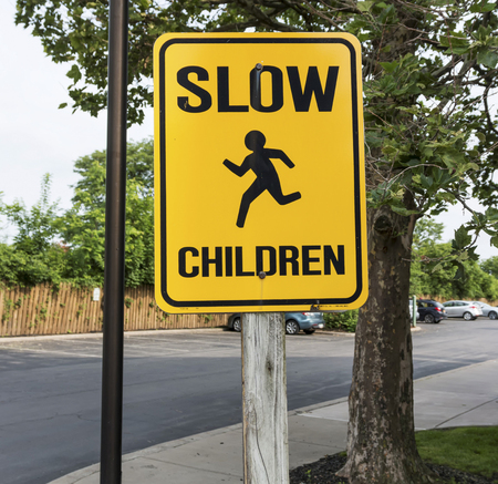 A yellow sign warning drivers to slow down  because children are around in a parking lot.の写真素材