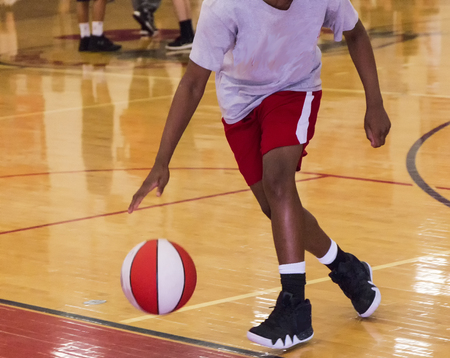 A young black male is dribbling a basketball indoors during summer basketball camp.の写真素材