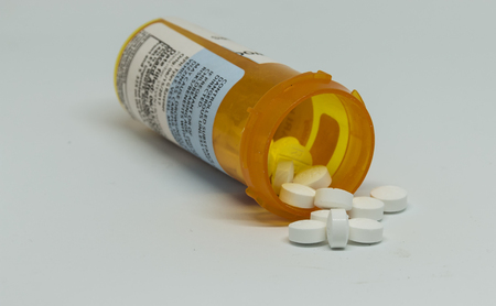 Pill bottle on its side with controlled substance pills falling out of the bottle with a white background.の写真素材