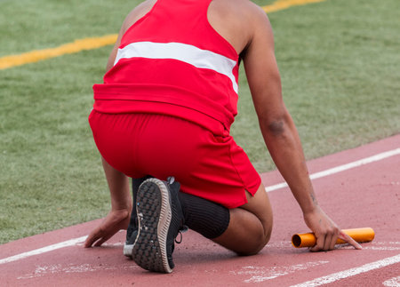 A high school runner is in the on your mark position ready to start a relay race at a track and...