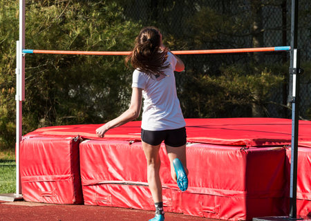 A young high school girl is approaching the high jump matts during a competition at a track and...