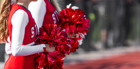 Two high school cheeleaders with red and white pom poms at a football game in autumn.の写真素材