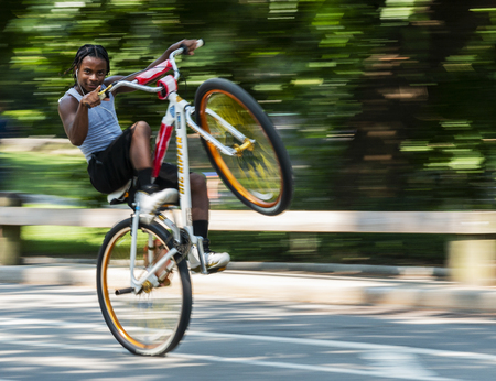Central Park, New York, USA - 15 August 2018: A young man is popping a wheelie showing off to the camera in Central Park New York City with a blurred backgound.のeditorial素材