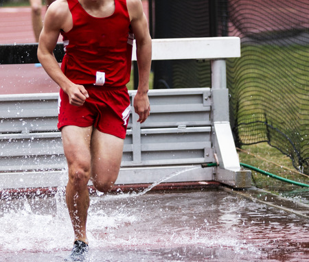 A high school boy is running out of the water jump during a steeplechase race in spring track and field.の写真素材
