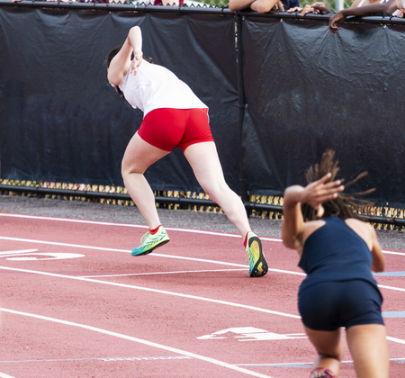 Two high school femal sprinters are starting a race in lanes four and five on a red track during a track and field sprint race.の写真素材