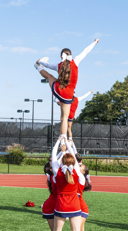 Cheerleaders in a pyramid practicing holding their teammate up by thieir ankles before homecoming.のeditorial素材