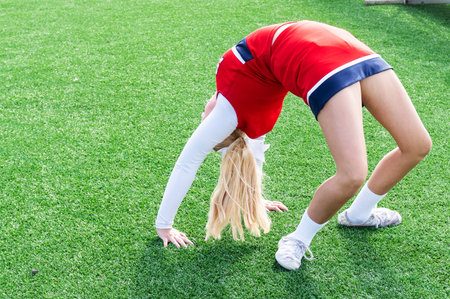 A high school cheerleader is in a bridge while warming up doing a back walk over on gree turf.