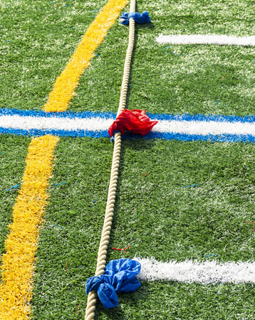 A tug of war rope with blue and red markers on it lying on a green turf field ready for the next game.の写真素材