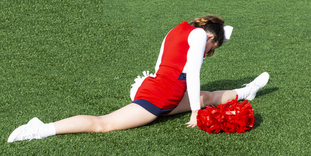 A high school cheerleader is in a split on a green turf field weaing a red, white and blue outfit.のeditorial素材