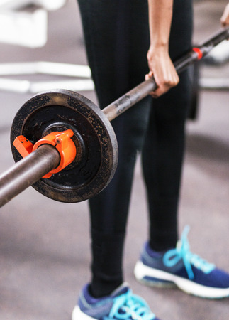 A young high school female track runner is learning how to do cleans while lifting weights in the weightroom.の写真素材