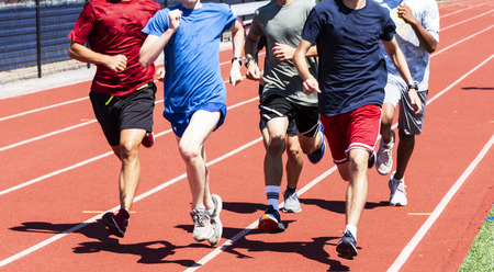 A boys high school team is running  in a group fast on a track during track and field practice.の写真素材