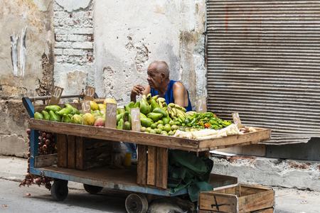 Havana, Cuba - 25 July 2018: A man sitting behind his fruit cart smoking a cigarette while selling fruit on the streets of Havana Cuba.のeditorial素材