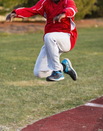 An african american triple jumper is in phase three of the hop, skip and jump during track and field practice outdoors in the winter.の写真素材