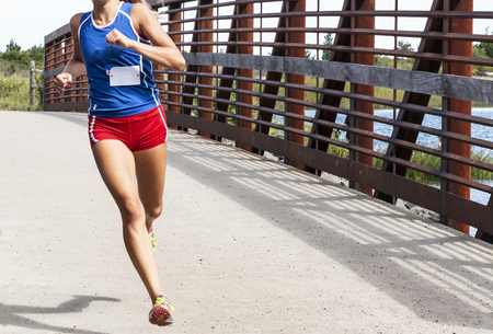 A high school cross country girl is running a race crossing a bridge wearing red shorts and blue racing top.の写真素材