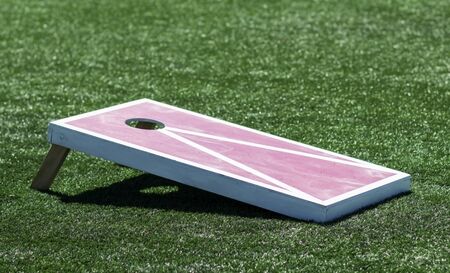 A red and white homemade wooden cornhole board is on a green turf field.の写真素材