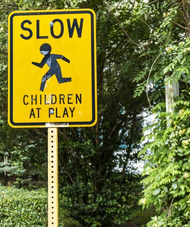 A yellow sign warning drivers that there are children at play in they neighborhood.stands on the side of the road.の写真素材