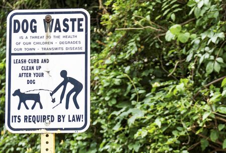 A sign on the side of the road reminding people to clean up after the dog and to have them on a leash.の写真素材